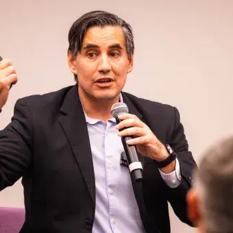 Luis Enrique Portales, durante su intervención en la entrega de reconocimientos NOVUS, explica el impacto de la innovación educativa mientras sostiene un micrófono y dialoga con el público asistente.