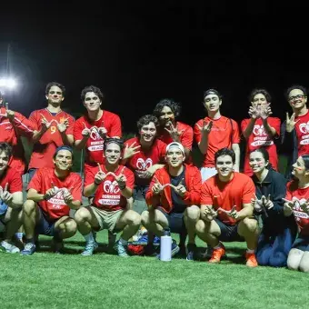 Grupo de jóvenes vestidos de rojo posando juntos en una cancha de fútbol. 