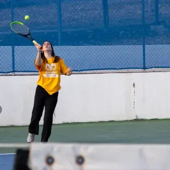 Alumna vestida de amarillo jugando tennis. 