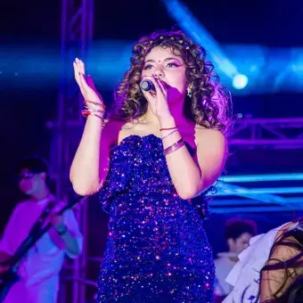 Cantante con vestido azul sobre el escenario, sosteniendo un micrófono.